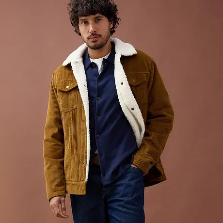 Bruine corduroy jas met lammy kraag over blauwe trui.