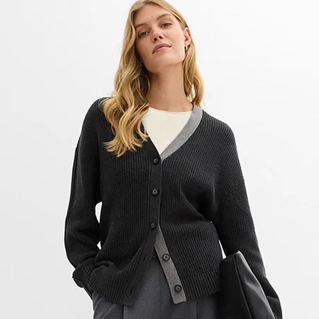 Donker gebreid vest over wit shirt, gecombineerd met grijze rok en zwarte tas.