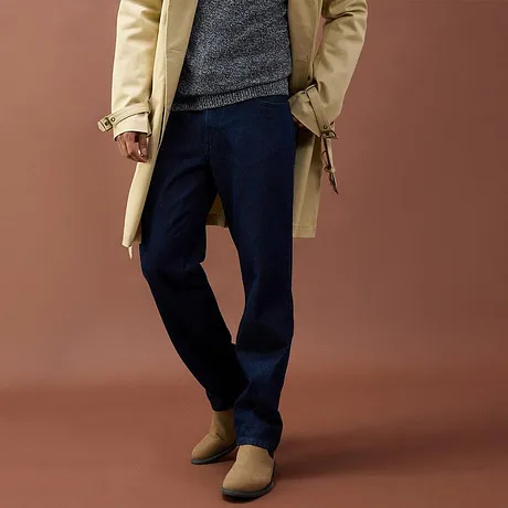 Lange beige jas, grijze trui, donkere broek en bruine schoenen.