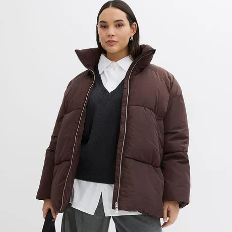 Bruine winterjas met hoge kraag met donkere trui en witte overhemdblouse eronder.