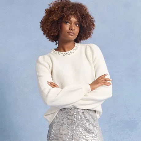 Witte trui met siersteentjes bij de kraag, gecombineerd met glinsterende zilverkleurige rok.
