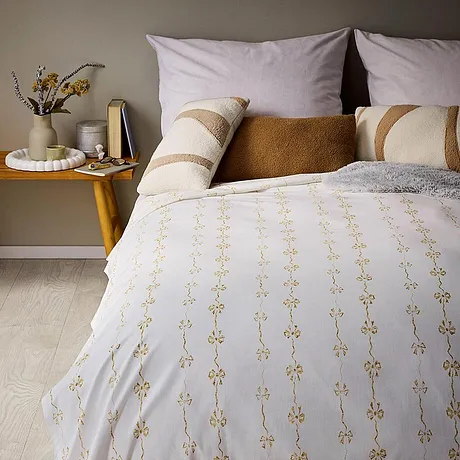 Wit dekbedovertrek, goudkleurig motief en meerdere sierkussens.