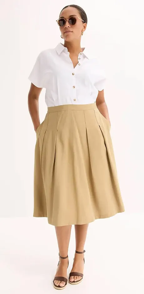 Elegante zomerlook: Wit kortarmig shirt gecombineerd met een beige midirok en zwarte sandalen.