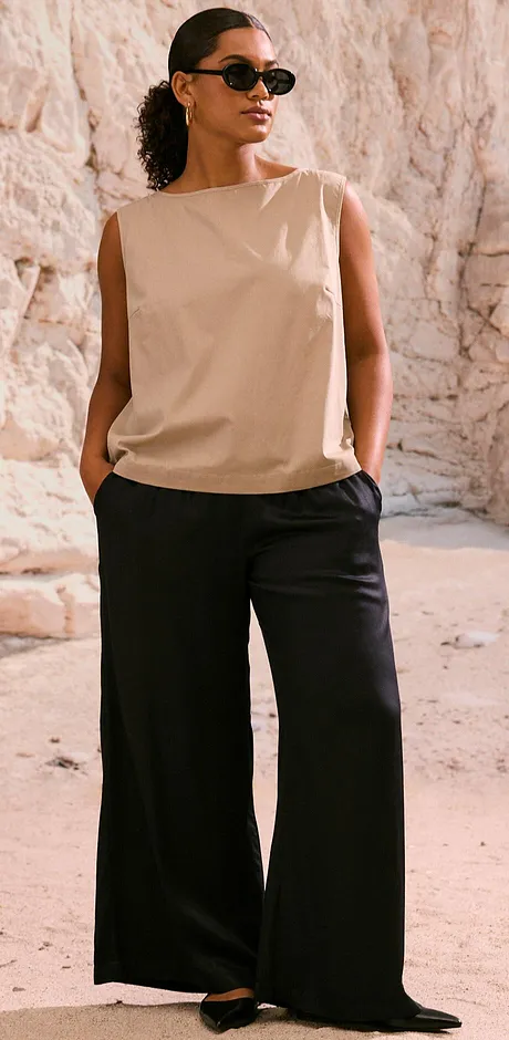  Kombination aus beigem ärmellosen Top und weiter schwarzer Hose. Stilvolle Sonnenbrille rundet den Look ab.