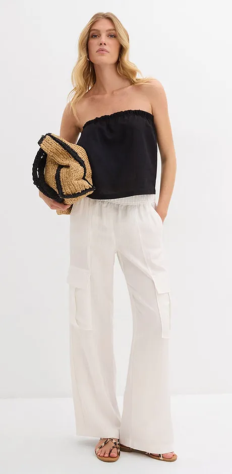 Sommerliches Outfit mit schulterfreiem schwarzem Top, weißer Leinenhose und geflochtenem Strohhut.