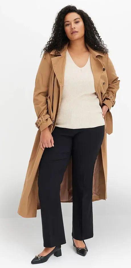 Klassieke beige trenchcoat over een wit topje en een donkere broek.