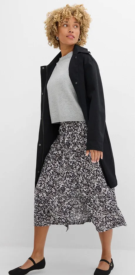 Elegante zwarte mantel, grijze trui en lange, met patronen versierde rok gecombineerd met platte schoenen.