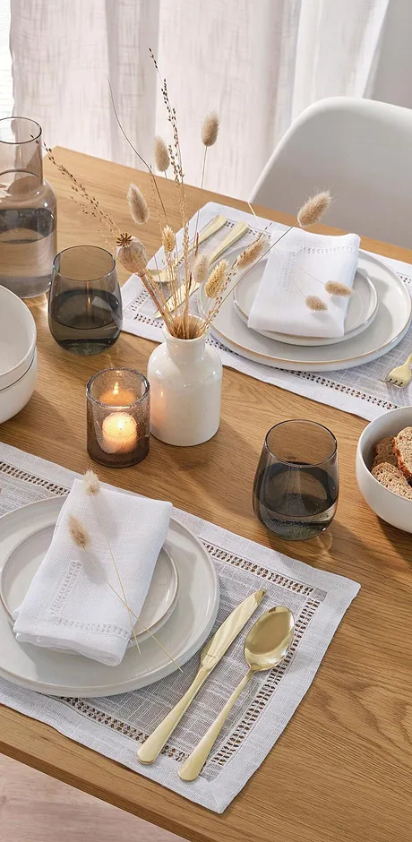 Witte stoffen servetten liggen elegant op gestructureerde placemats, omringd door eenvoudige borden en bestek.