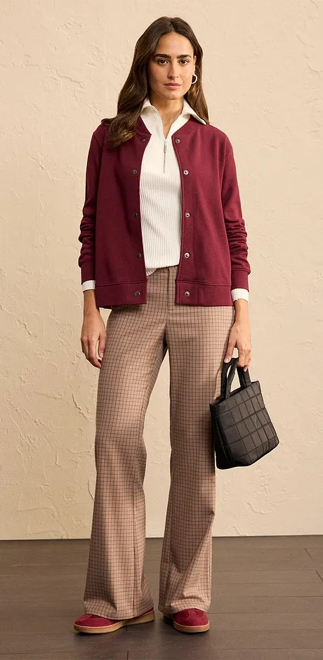 Combinatie van een wijnrode gebreide cardigan, witte blouse en geruite broek.