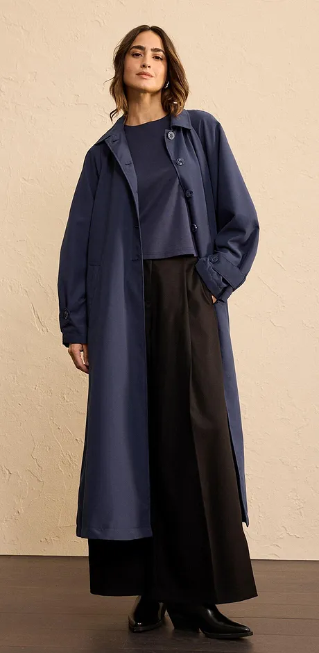 Elegante lange jas in donkerblauw, gecombineerd met wijde broek en eenvoudige top.