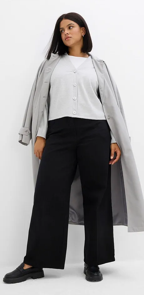 Grijze jas over een witte blouse en een wijde zwarte broek.