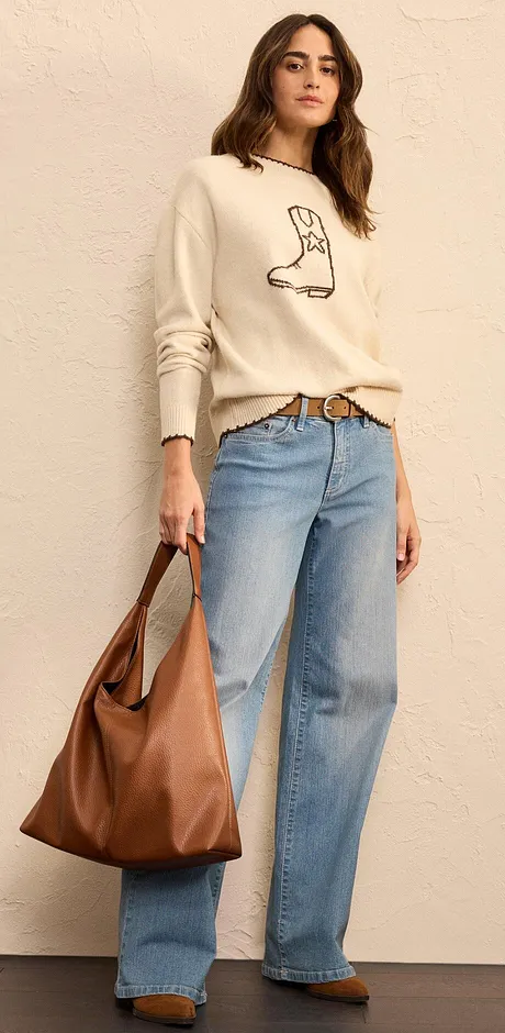 Crèmekleurige trui met laarzen print, wijde jeans en een grote, bruine leren tas.