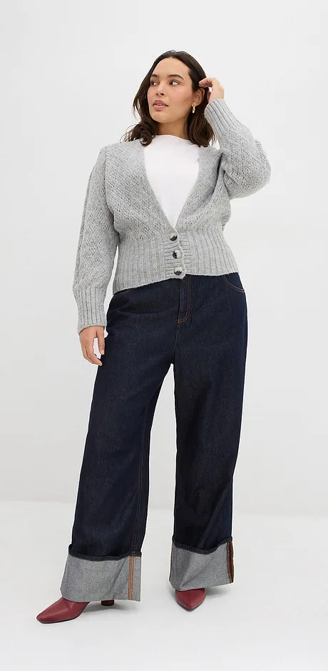 Grijs vest over witte top, donkere jeans met omslag en rode schoenen.