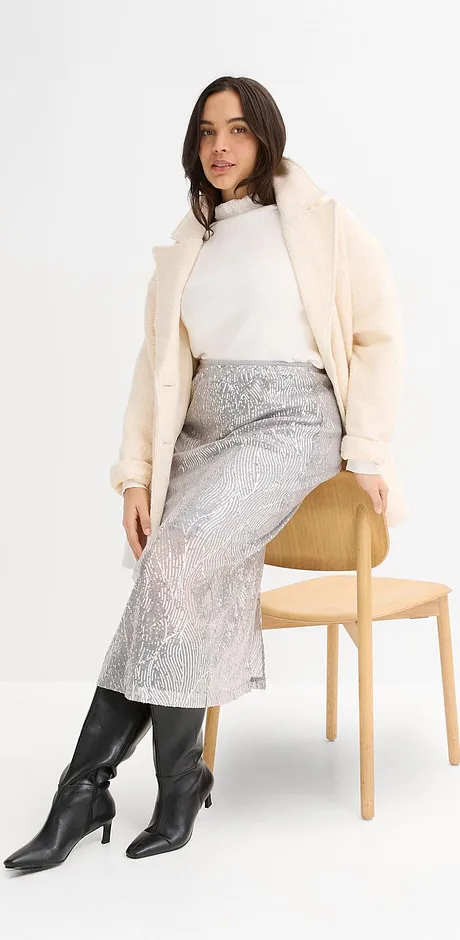 Crèmekleurige lange jas, witte coltrui, zilverkleurige rok en zwarte imitatieleren laarzen.