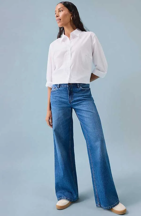 Wit overhemd bij blauwe jeans met wijde pijpen en witte schoenen.