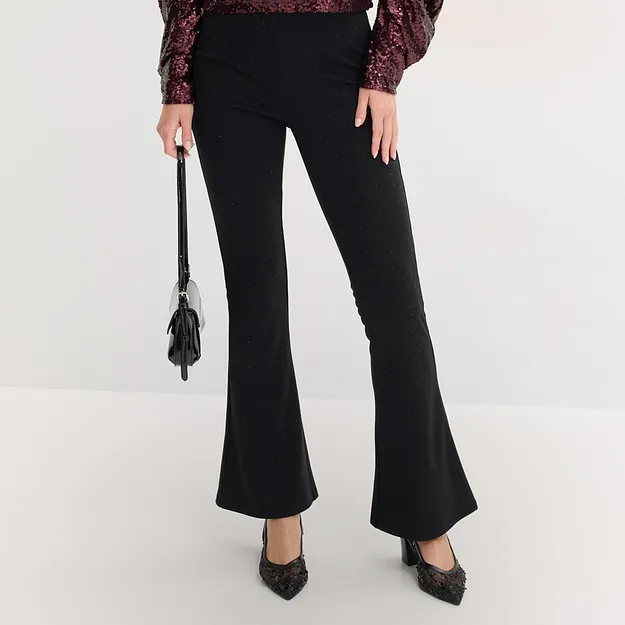 Elegante zwarte flared broek gecombineerd met blouse met pailletten en pumps met spitse neus.