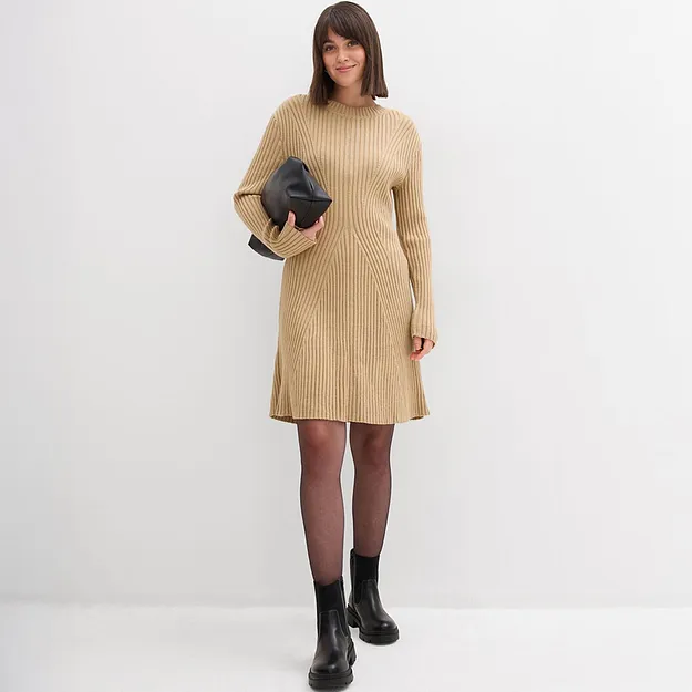 Elegante gebreide jurk in beige met ronde hals en lange mouwen met een zwarte clutch erbij.