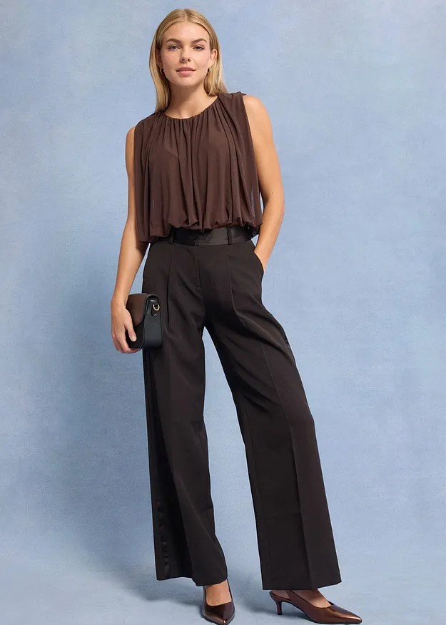 Bruine mouwloze top en wijde, donkere broek.