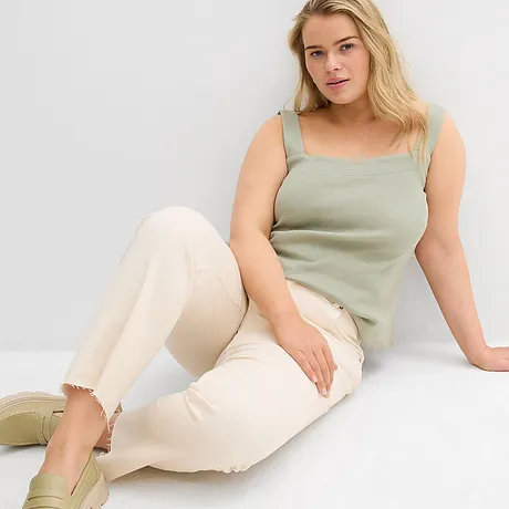 Grünes Top mit breiten Trägern, helle Jeans mit ausgefranstem Saum und pastellfarbene Schuhe.