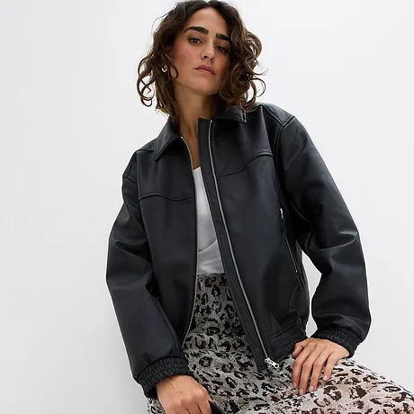 Zwarte jas van imitatieleder met ritssluiting, gecombineerd met een wit shirt en een rok met patroon.