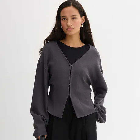 Elegant grijs gebreid vest over een zwart topje. Casual look met V-hals en knopenrij.