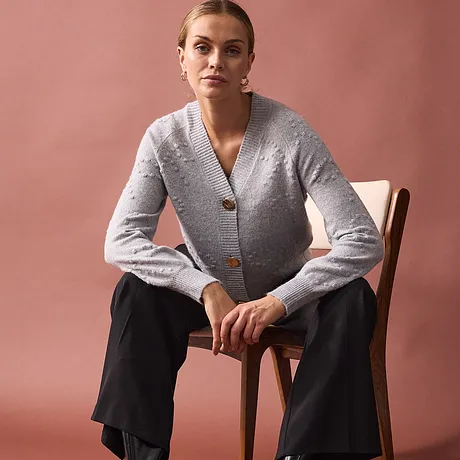 Elegant gebreid vest in grijs met grote knopen, gecombineerd met zwarte broek.