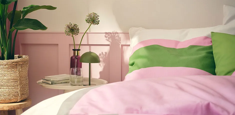 Pastelkleurige bedlinnen in roze en groen siert het gezellige bed in de zonovergoten slaapkamer.