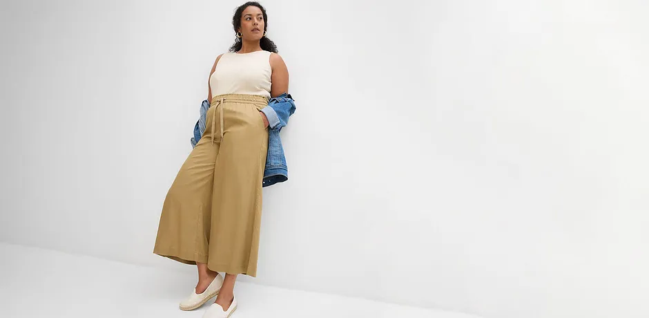Ontspannen zomerlook: wijde beige broek, wit topje en een los blauw spijkerjack.