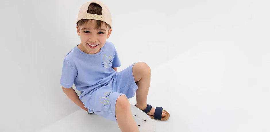 Lichtblauw T-shirt en korte broek met schattige borduursels, beige baseballpet en donkerblauwe sandalen.