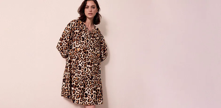 Ein luftiges Kleid mit Leopardenmuster fällt locker über die Schultern und endet knapp überm Knie.