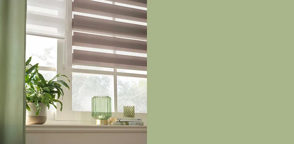 Mooie raambekleding met plisségordijnen in aardetinten. Groene decoraties en kamerplanten zorgen voor een natuurlijke sfeer.