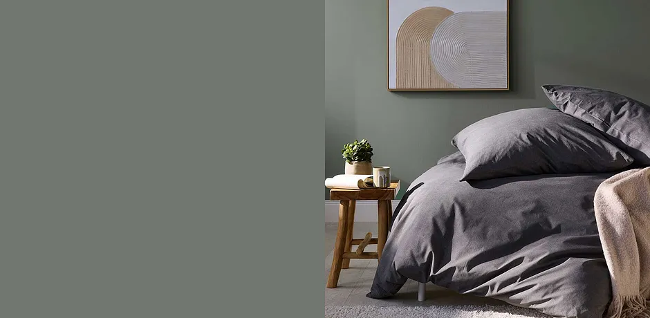 Elegante grijze dekbedovertrekken harmoniëren met de groene muur. Een plant complementeert de eenvoudige sfeer in de slaapkamer.