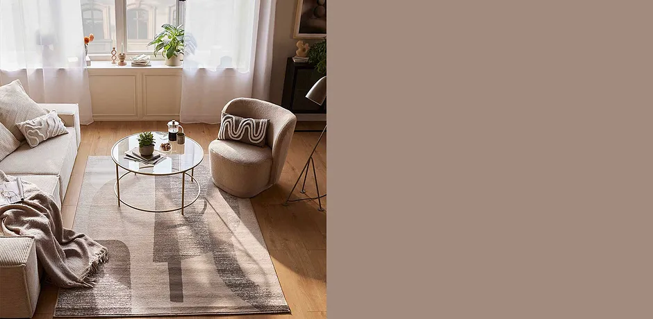 Gezellige woonkamer met beige fauteuil, donzige plaid en stijlvol vloerkleed in warme aardetinten.