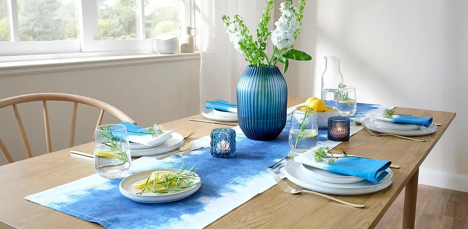 Een blauwe tafelloper siert de eettafel, in contrast met witte borden en kleurrijke accessoires.