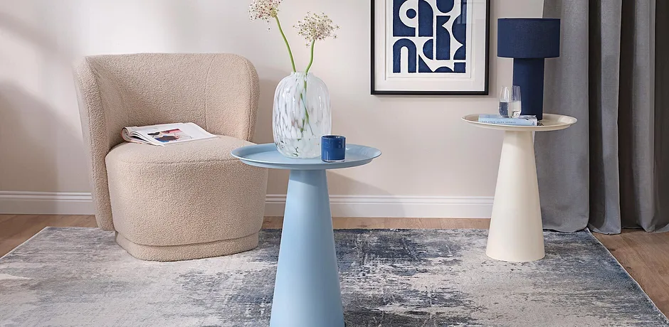 Moderne woonruimte met een crèmekleurige fauteuil en lichtblauwe bijzettafels.