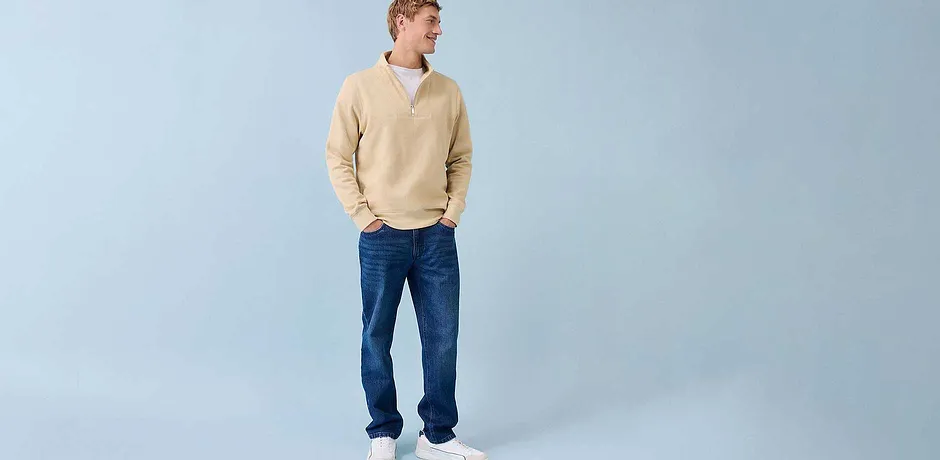 Casual look met een crèmekleurige trui, blauwe spijkerbroek en witte sneakers.