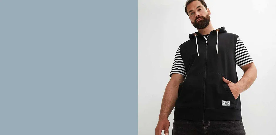 Mouwloos zwart sweatvest over een gestreept T-shirt.