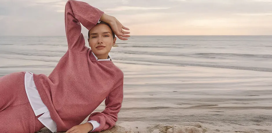 Dame in een roze gebreide hoodie bij de zee, een knusse loungewear-stijl.