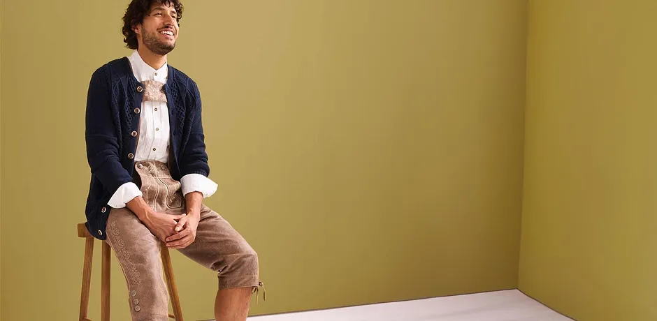 Marineblauw gebreid vest over een lichtblauw Tiroler overhemd, gecombineerd met een beige lederhose. 