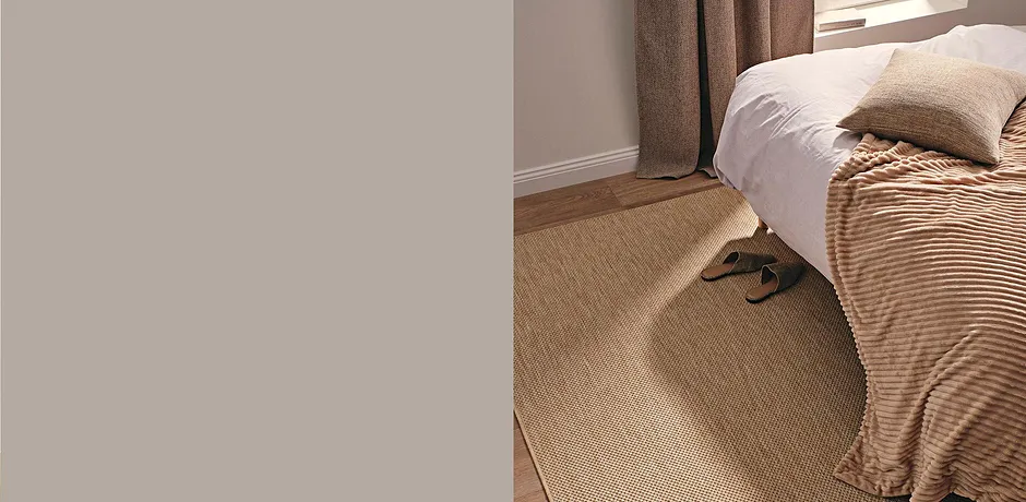 Casual pantoffels liggen op een vloerkleed van natuurlijk sisal naast een bed met een dekbedovertrek in corduroy look.