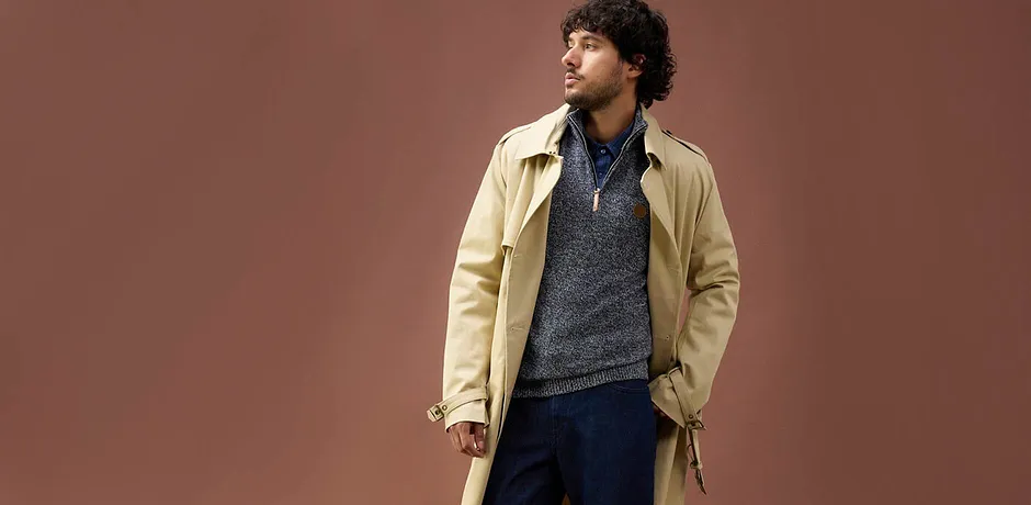 Beige trenchcoat over blauw-grijze trui met jeans - casual herfstlook voor koude dagen.