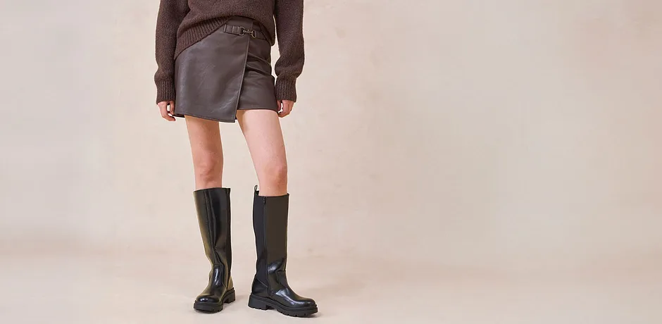 Imitatieleren rok en kniehoge laarzen gecombineerd met bruine trui.