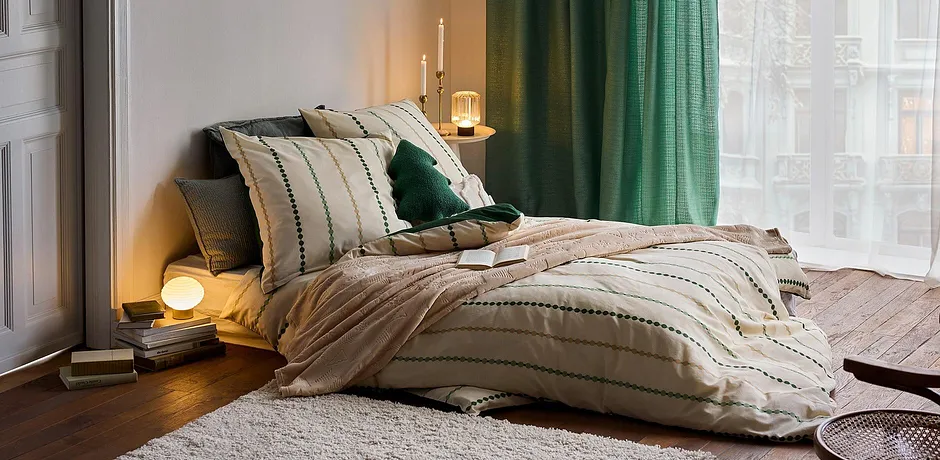Gestreept dekbedovertrek in beige, groene kussens en gordijn zorgen voor een behaaglijke sfeer.