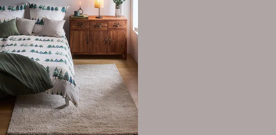 Comfortabel winter-dekbedovertrek met dennenboommotief, groene plaid en wollig vloerkleed voor een behaaglijke sfeer.