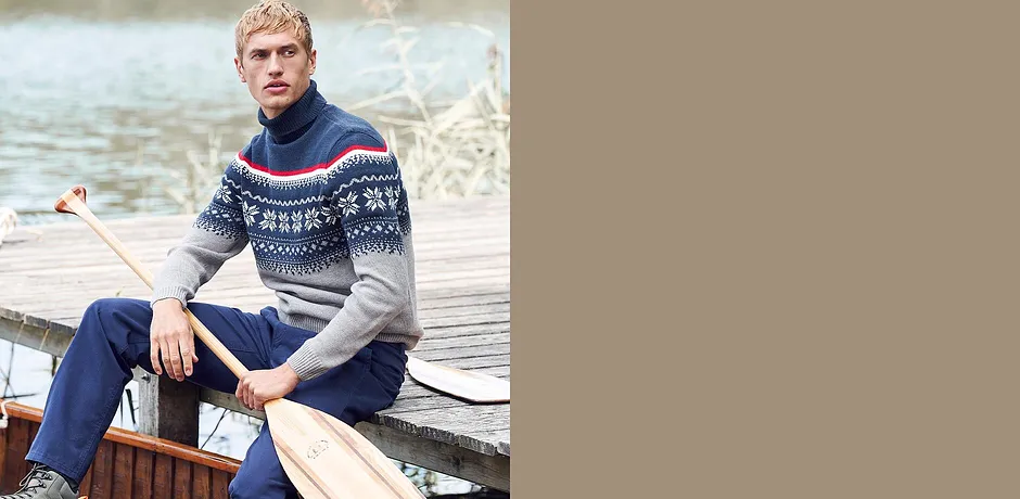 Man in trui met Noors patroon en jeans zit ontspannen op een boot.