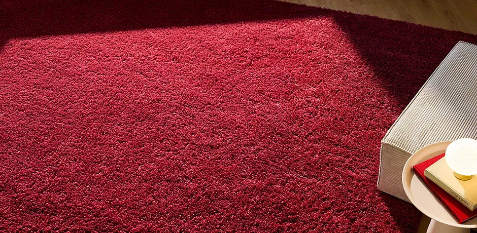 Felrood vloerkleed domineert de ruimte, met een opengeslagen boek op een lichte ondergrond ernaast.