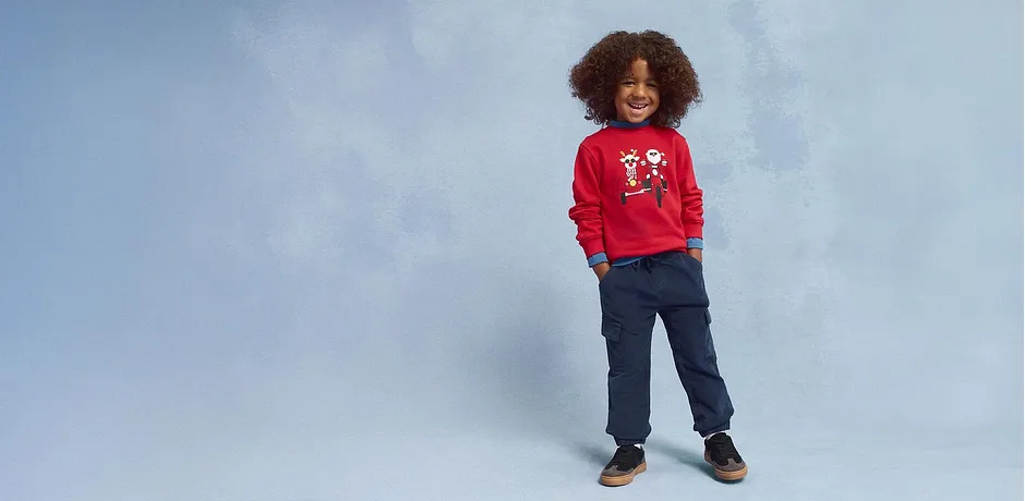 Rode trui met kerstmotief, blauwe broek en bruine schoenen.