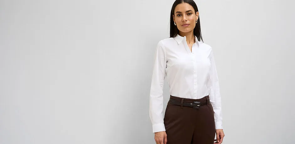 Witte blouse met opstaande kraag gecombineerd met elegante bruine broek.