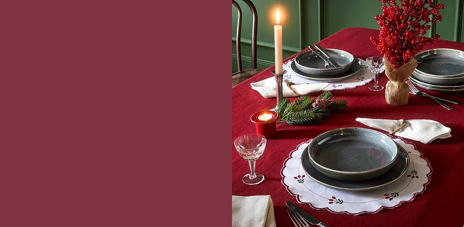 Feestelijke tafeldecoratie met rood tafelkleed, witte placemats en zilveren bestek.