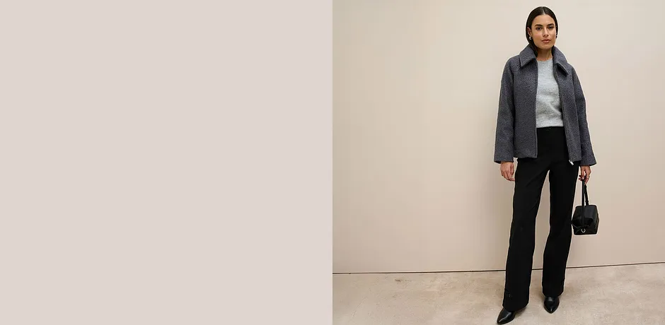 Grijze jas, lichtgrijze trui en zwarte broek.